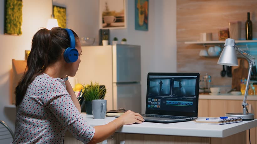 Freelancer content creator working overtime from home to respect deadlines. Woman videographer editing an audio film montage on a professional laptop sitting on the desk in a modern kitchen.