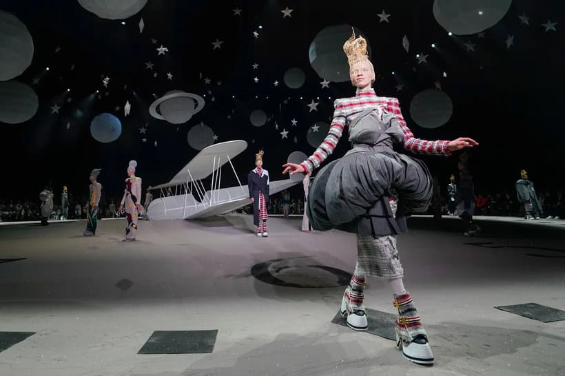 Models from Thom Browne’s show walling past a life-size biplane crash landed in a clock-shaped desert wearing bizarre red and grey knits. 